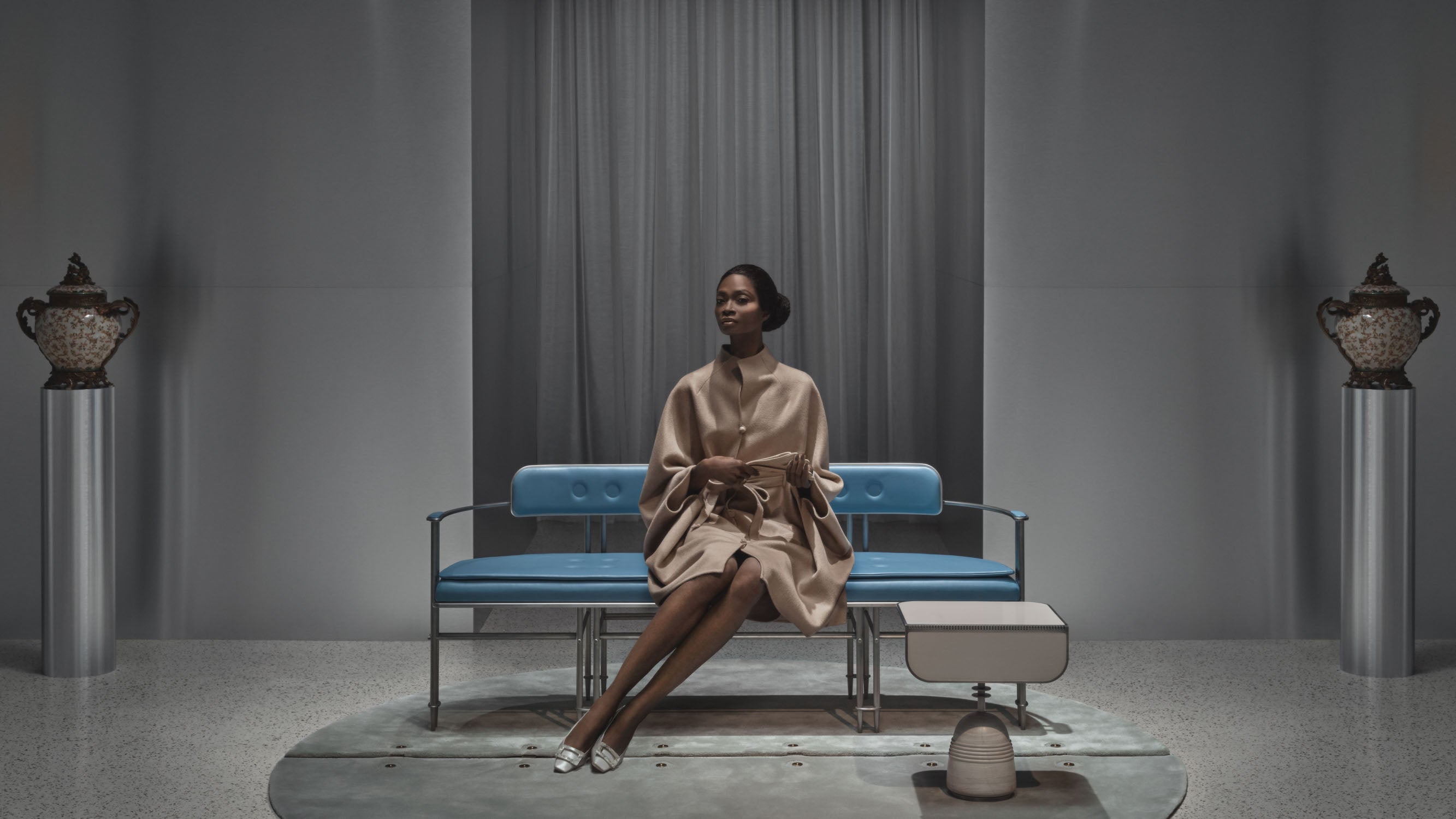 Woman in a beige dress sitting on a modern blue sofa in a minimalist room with two decorative urns on pedestals