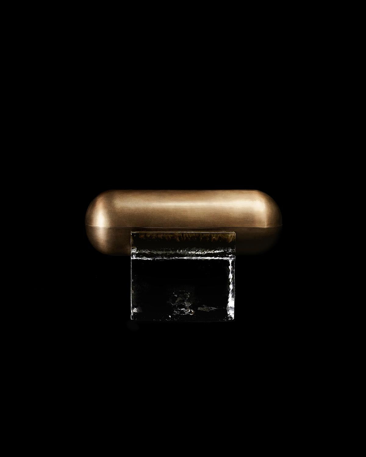 Close-up of a smooth metallic bronze capsule-shaped object resting on a clear textured rectangular block against a black background