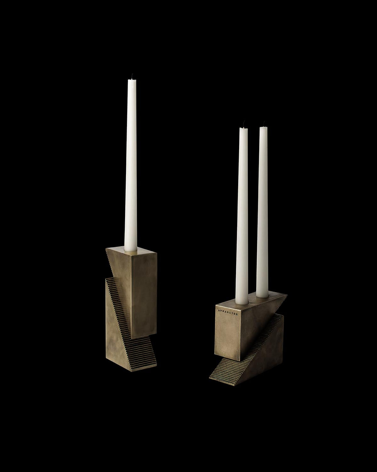 Pair of geometric bronze candle holders with long white taper candles against a black background