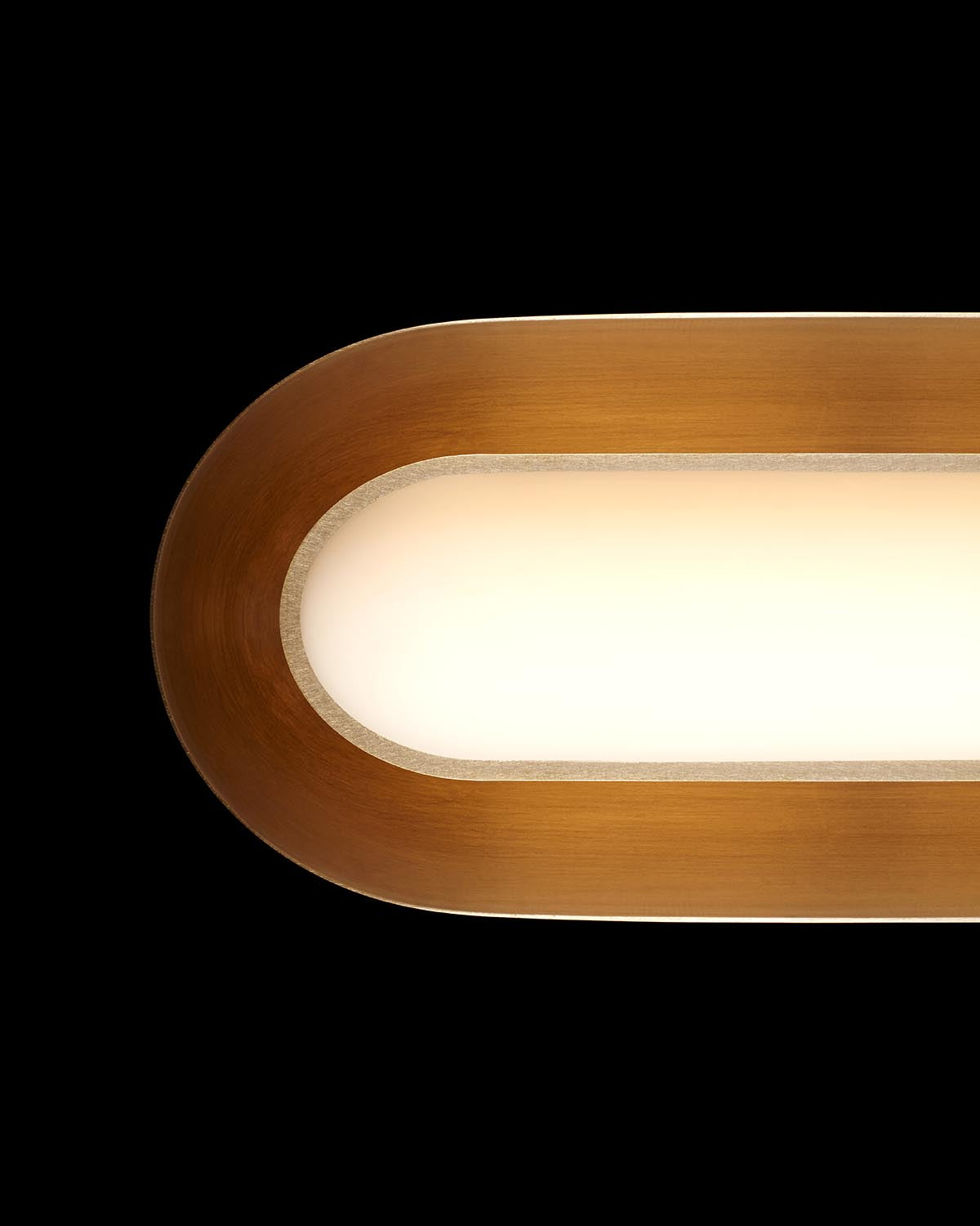 Close-up of elongated oval pendant light with warm bronze frame and diffused white glass shade on black background