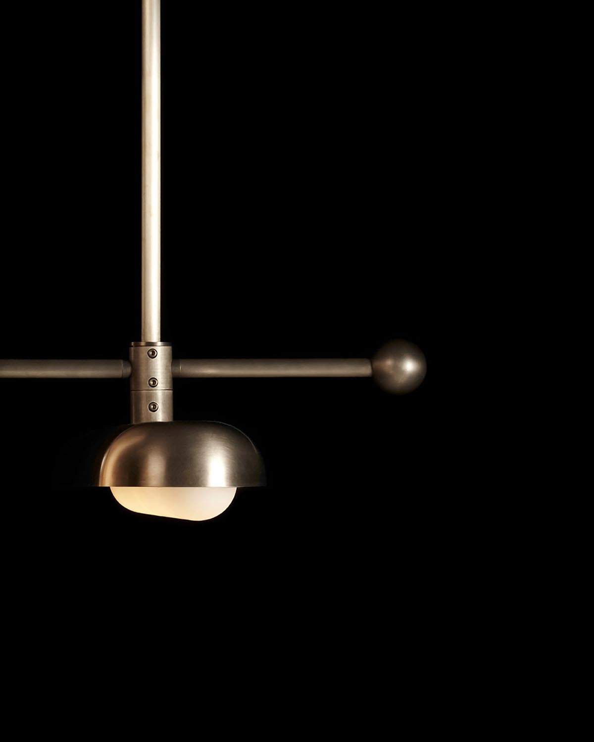 Close-up of a modern metal pendant light fixture with spherical end and dome-shaped diffuser against black background