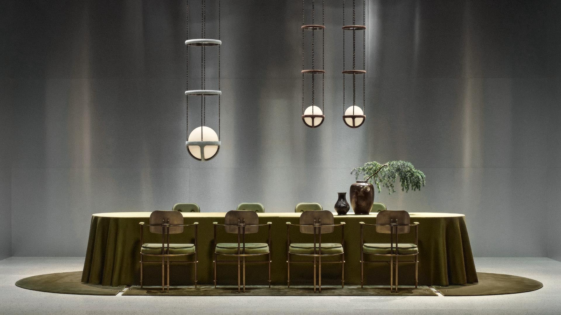 Minimalist dining area with an olive green tablecloth, six vintage chairs, three modern pendant lights, and decorative vases