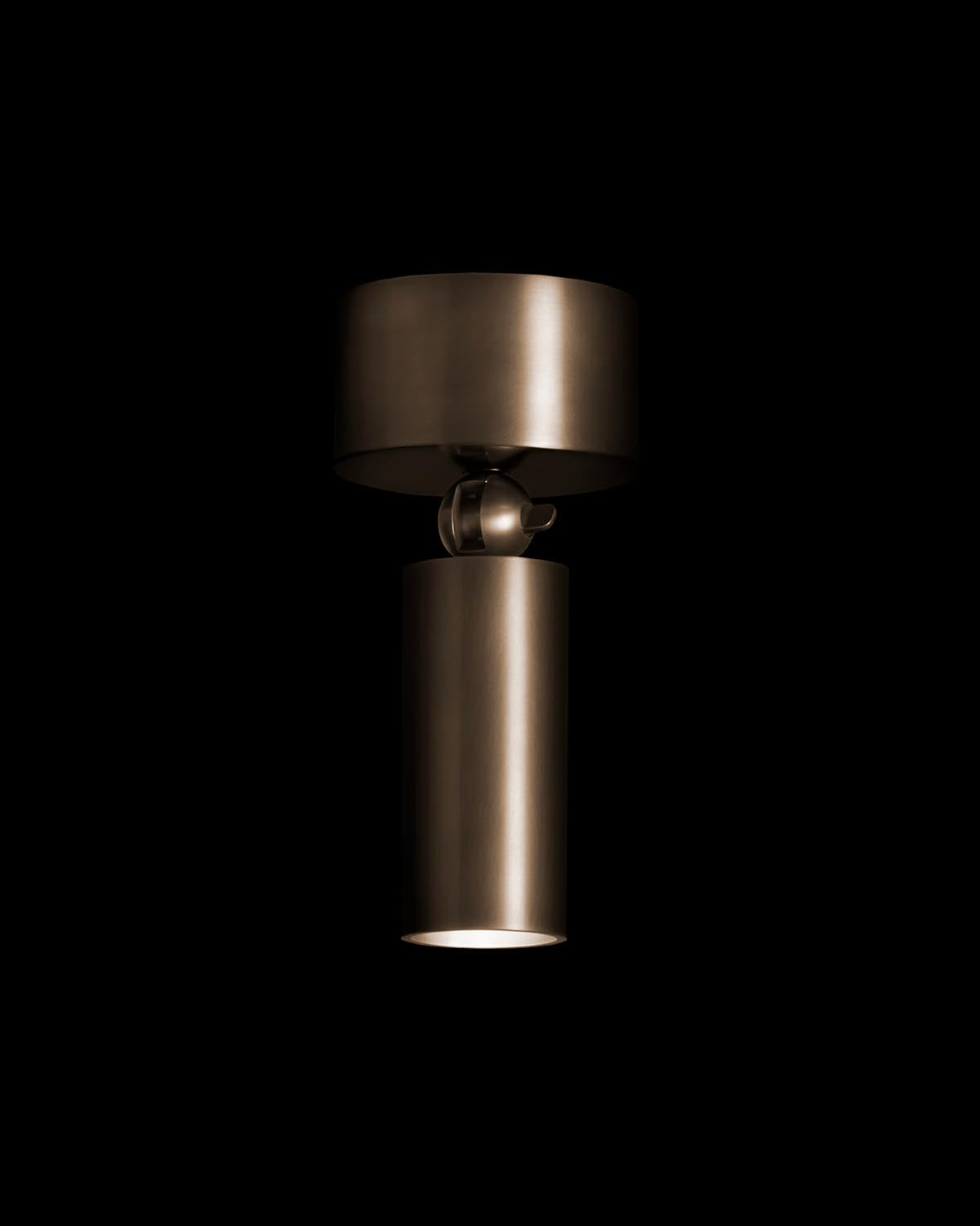 Close-up of a cylindrical downlight with matte bronze finish against a black background illuminating downward light