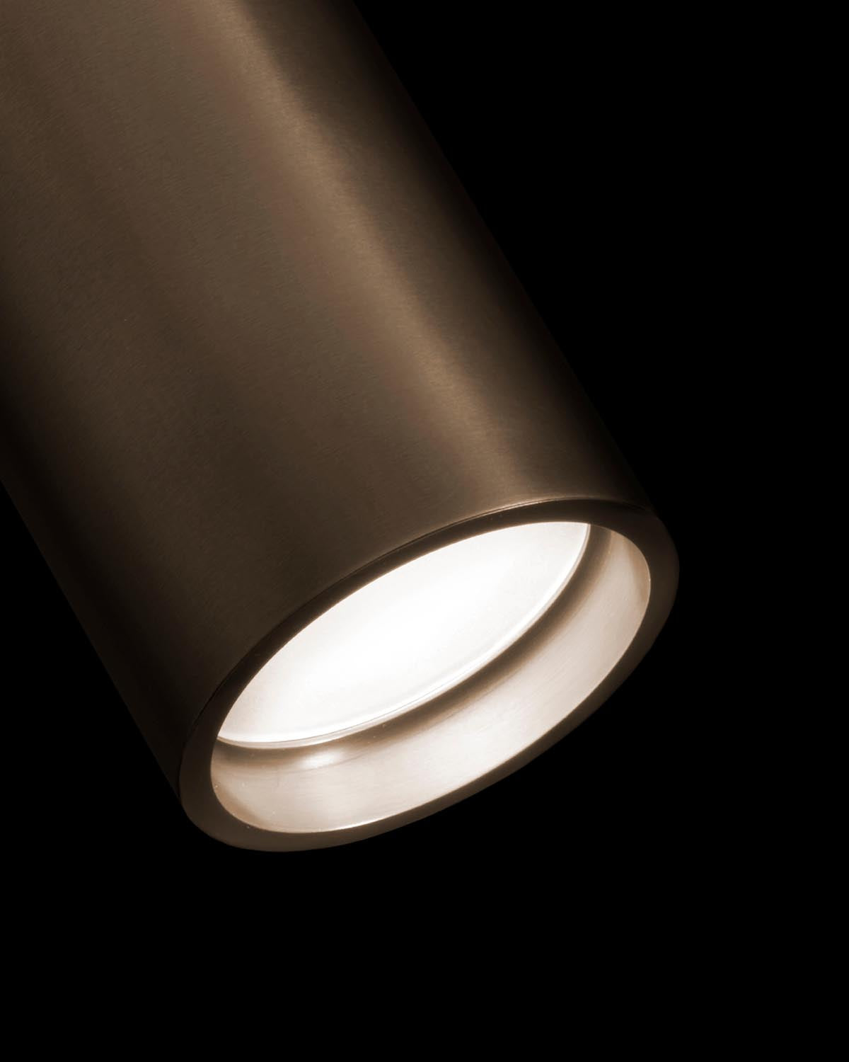 Close-up of a matte bronze cylindrical downlight fixture emitting soft white light on a black background