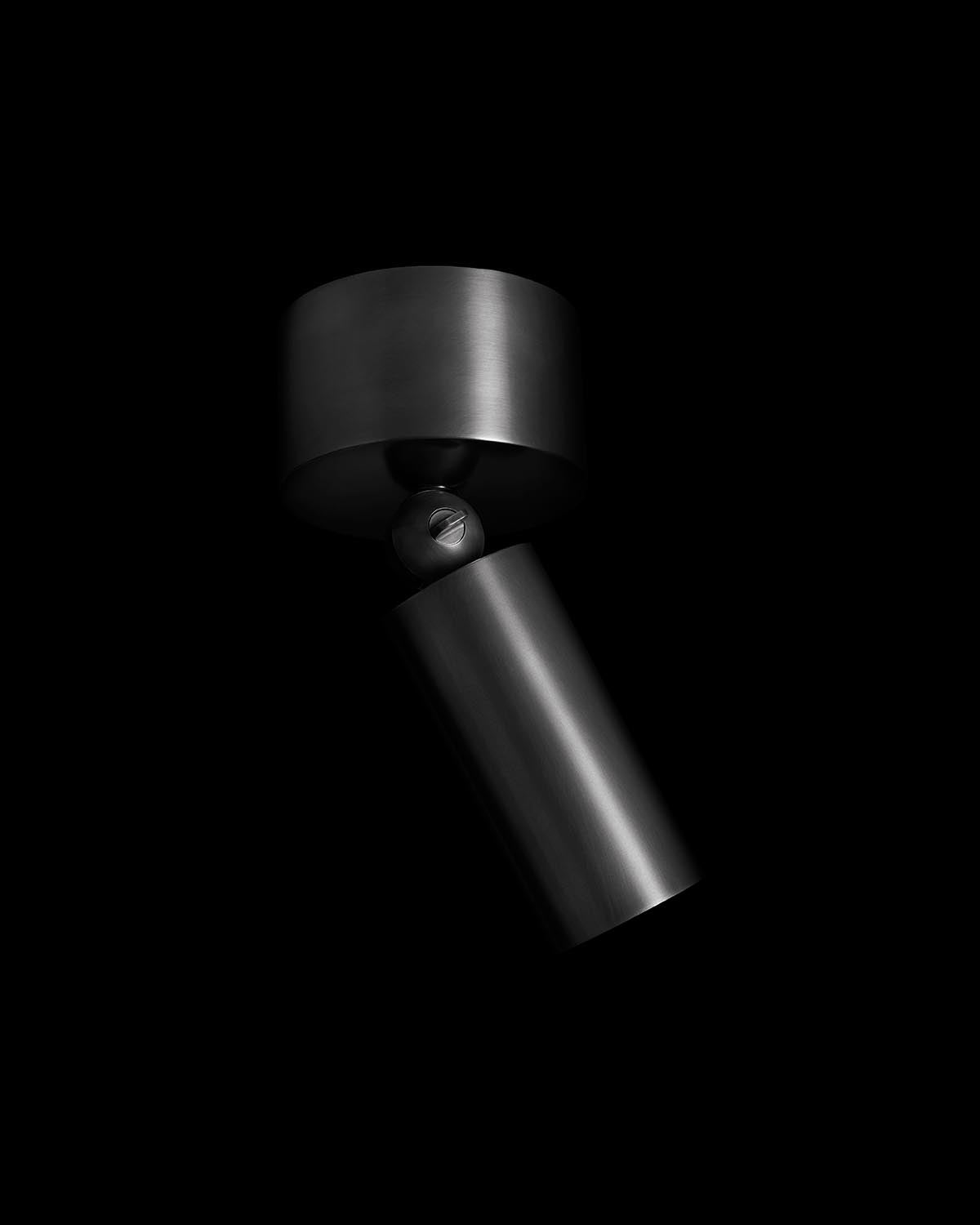 Sleek matte black cylindrical downlight fixture with adjustable joint against a deep black background