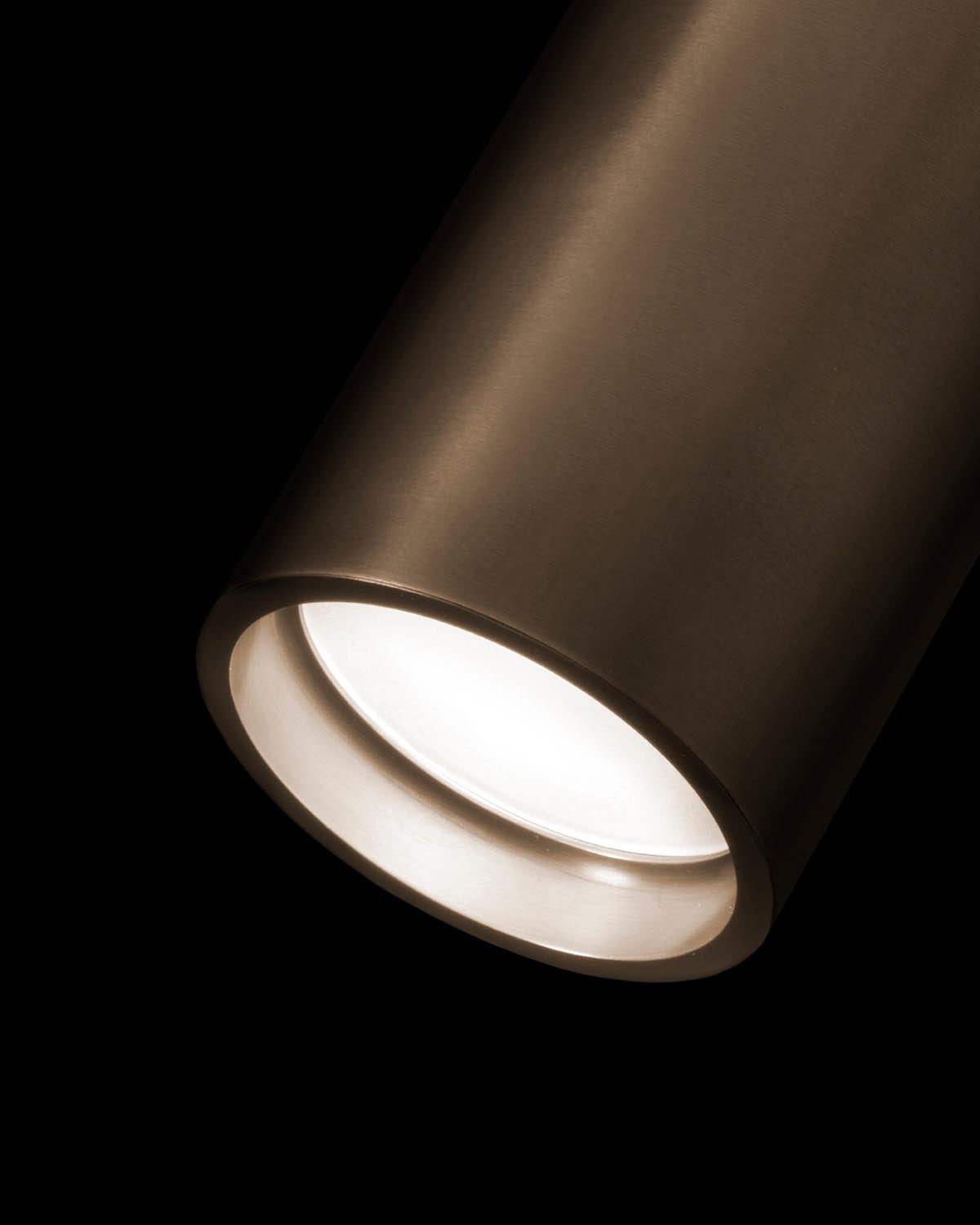 Close-up of a bronze cylindrical reading sconce with glowing light against a black background