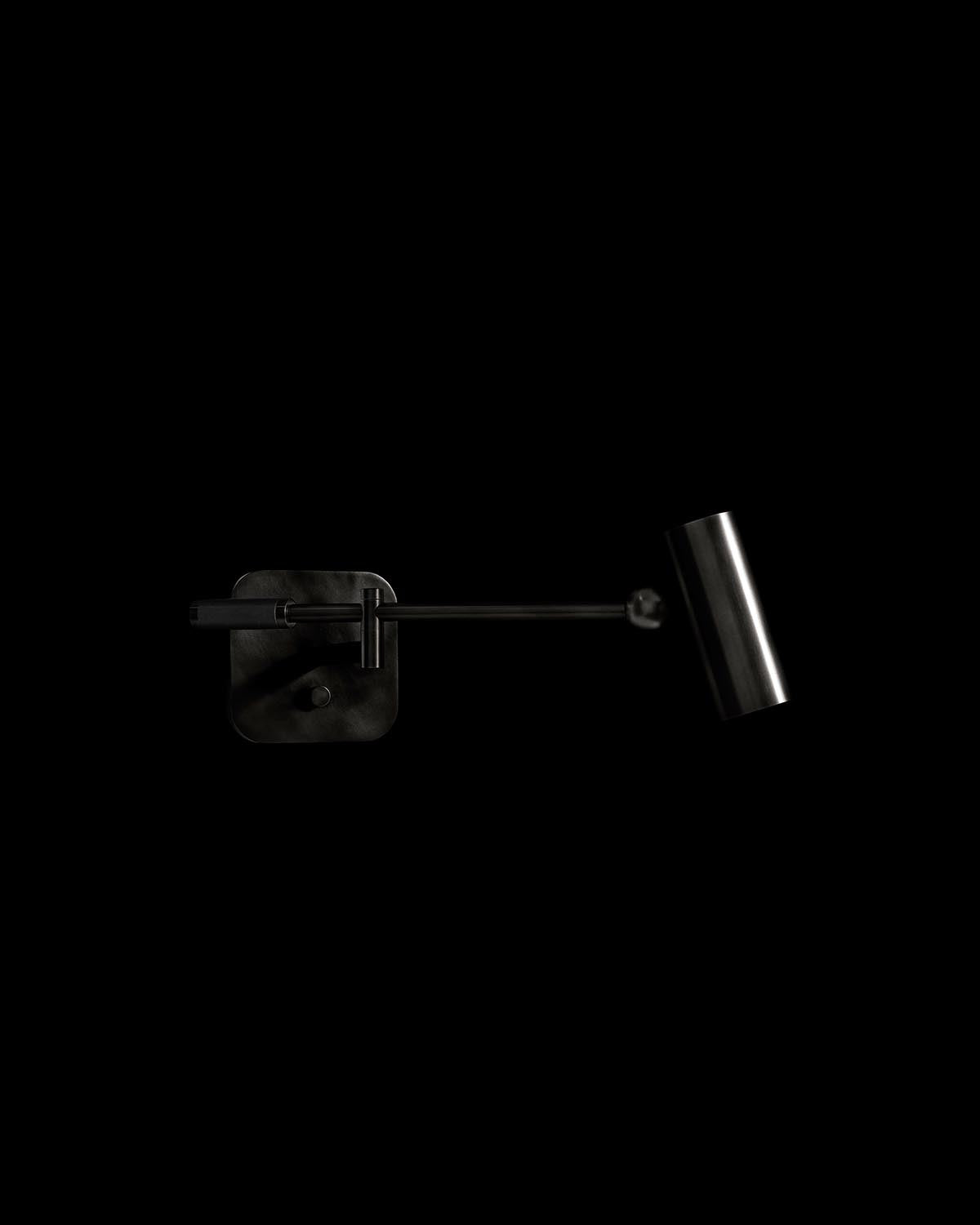 Minimalist black metal reading sconce with cylindrical lamp head and adjustable arm on a dark background