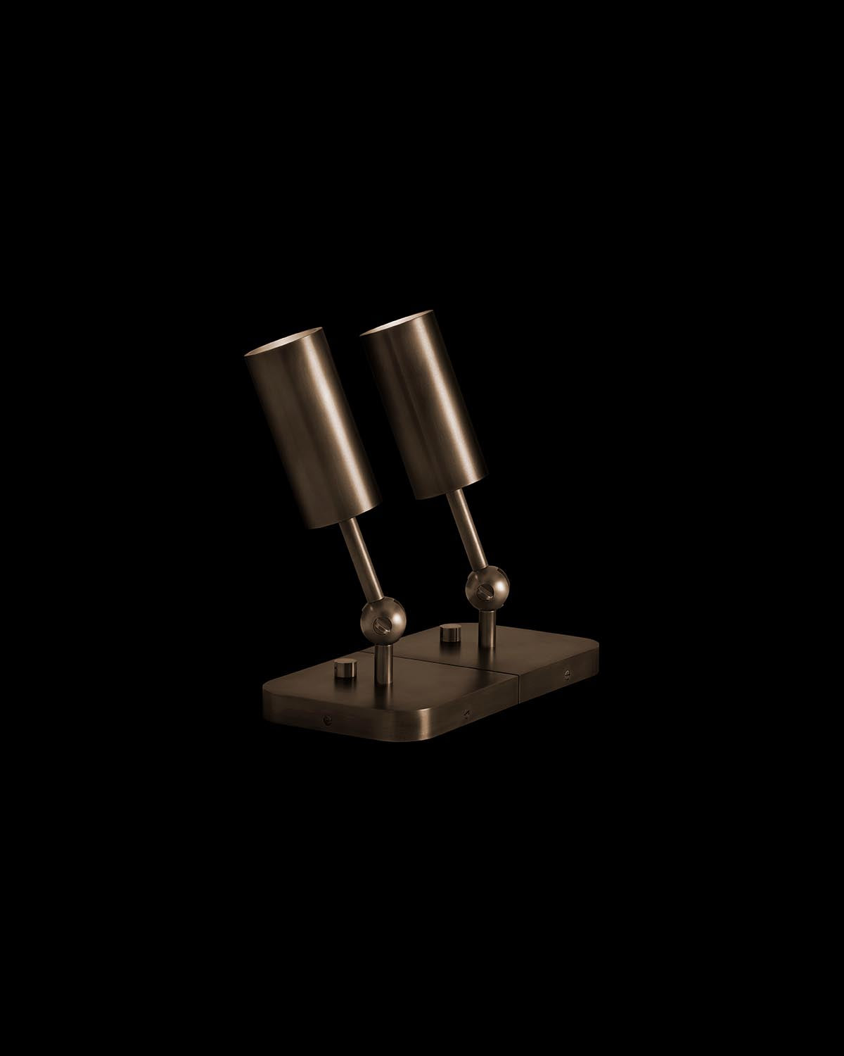 Close-up of dual cylindrical uplight fixtures with metallic finish mounted on a rectangular base against black background