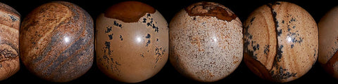 Close-up of polished round natural stone spheres with varied earthy brown and beige patterns against a white background