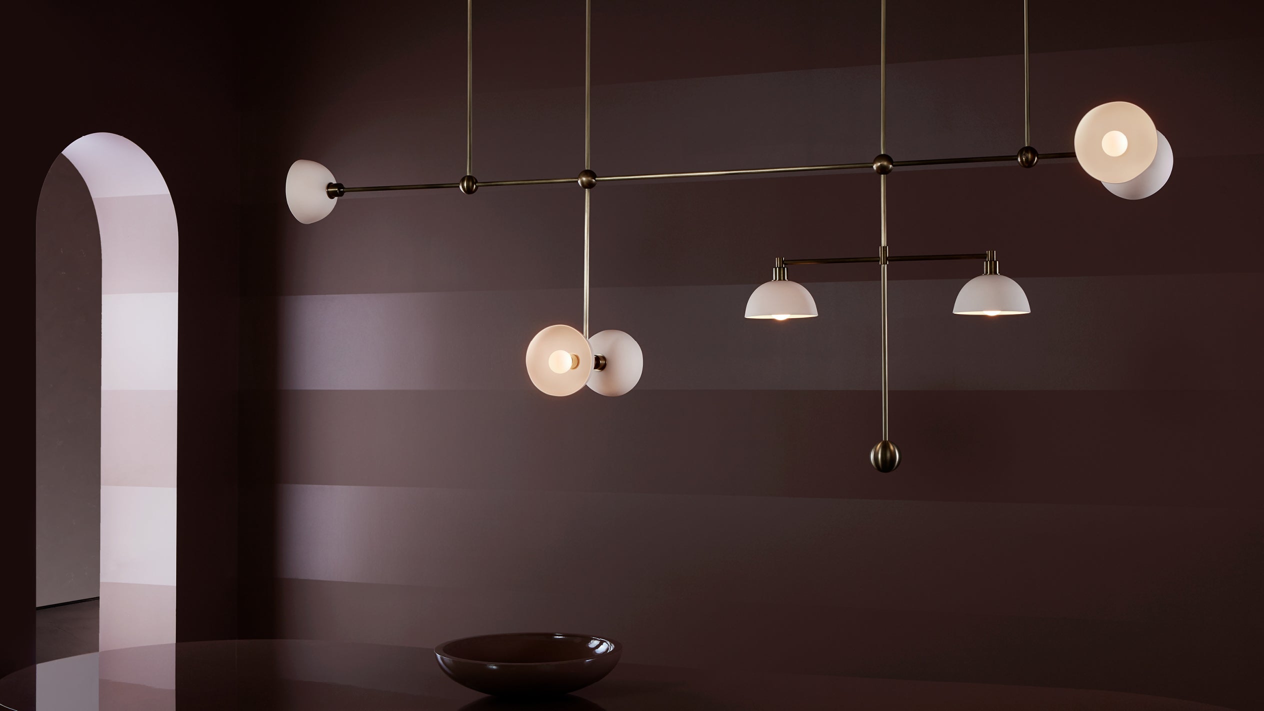 Minimalist interior with matte brown walls, a modern linear chandelier, and an arched doorway with soft lighting