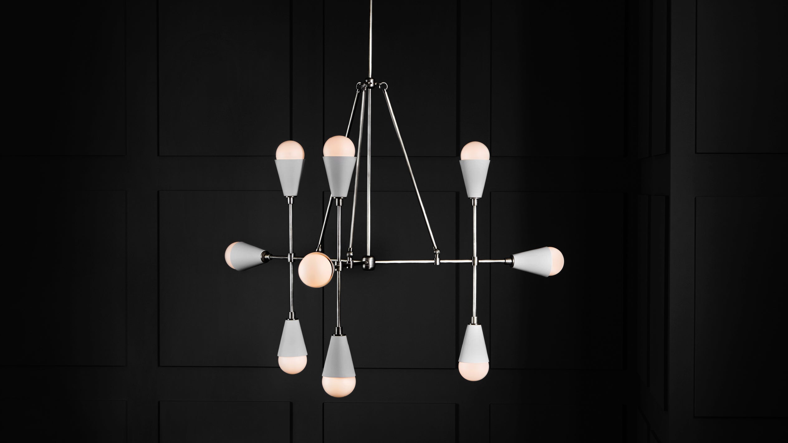 Modern geometric chandelier with eight white bulb-shaped lights and slender metal arms against a black paneled wall