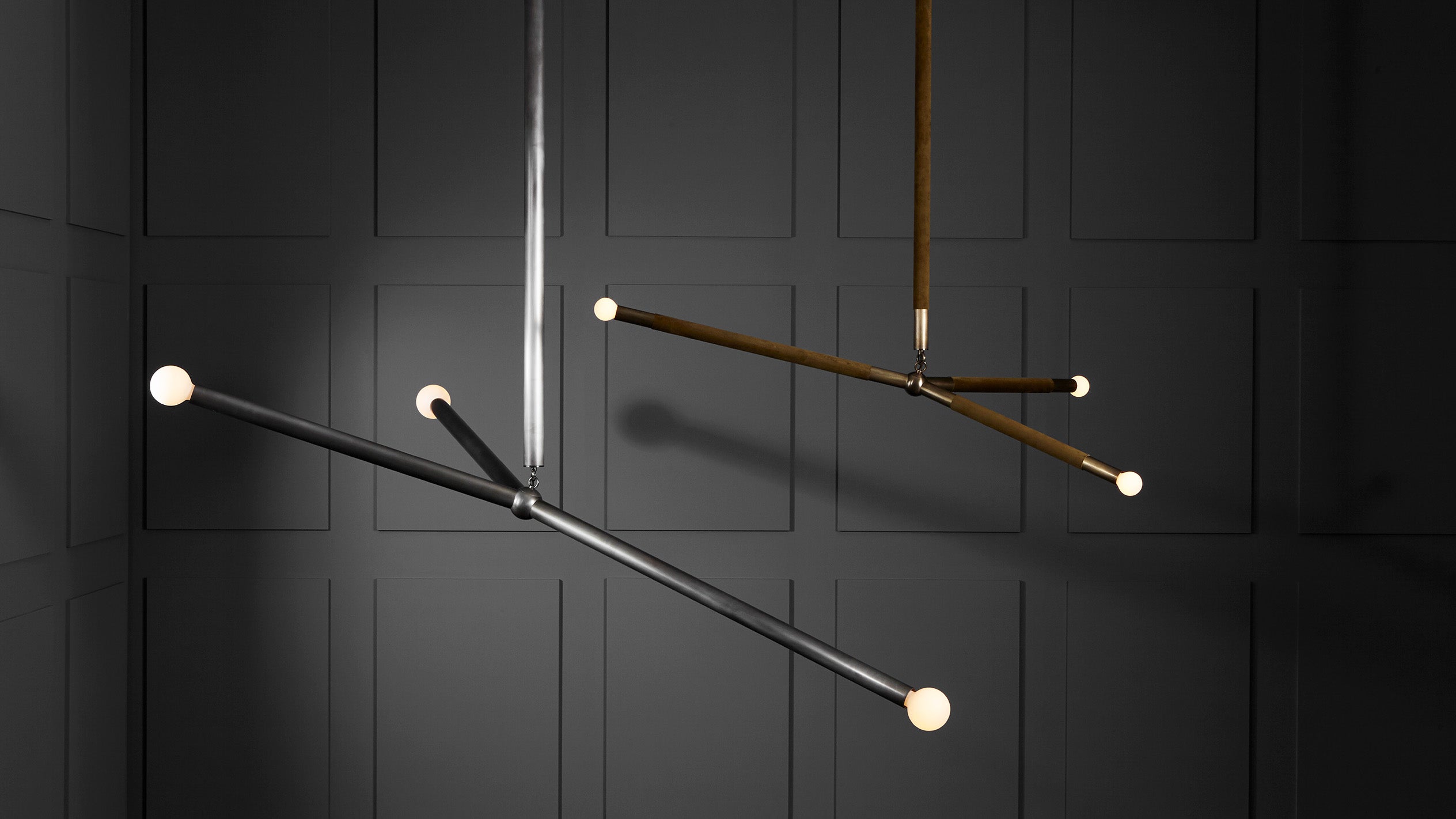 Two modern linear pendant lights with spherical bulbs hanging against a dark paneled wall background
