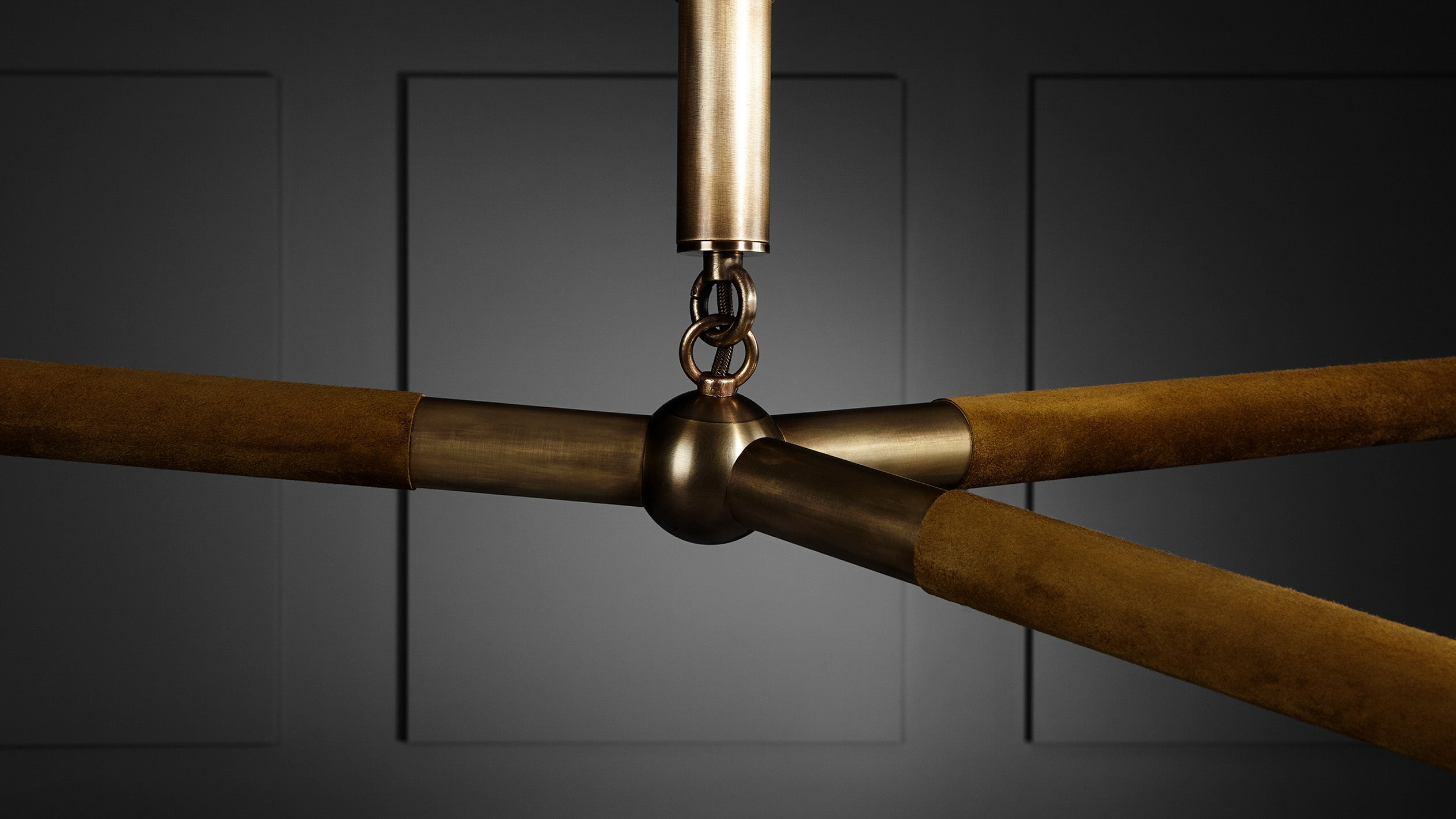 Close-up of antique brass and rust-colored metal rods connected by a joint against dark gray paneled wall