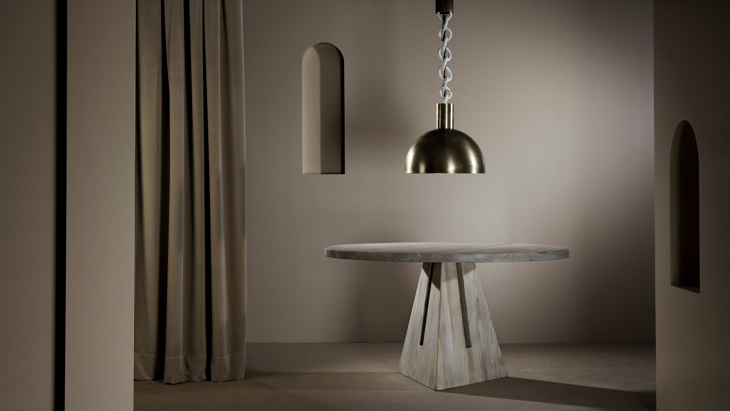 Round concrete table with geometric base under a metallic pendant light in a neutral-toned minimalist room