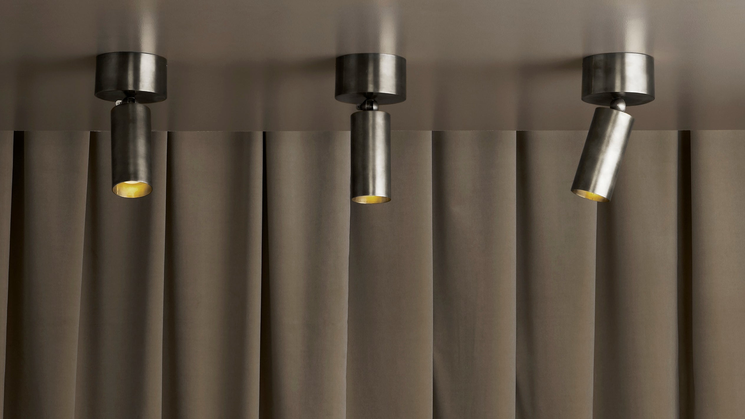 Set of three cylindrical black metal ceiling spotlights installed against a beige fabric curtain backdrop