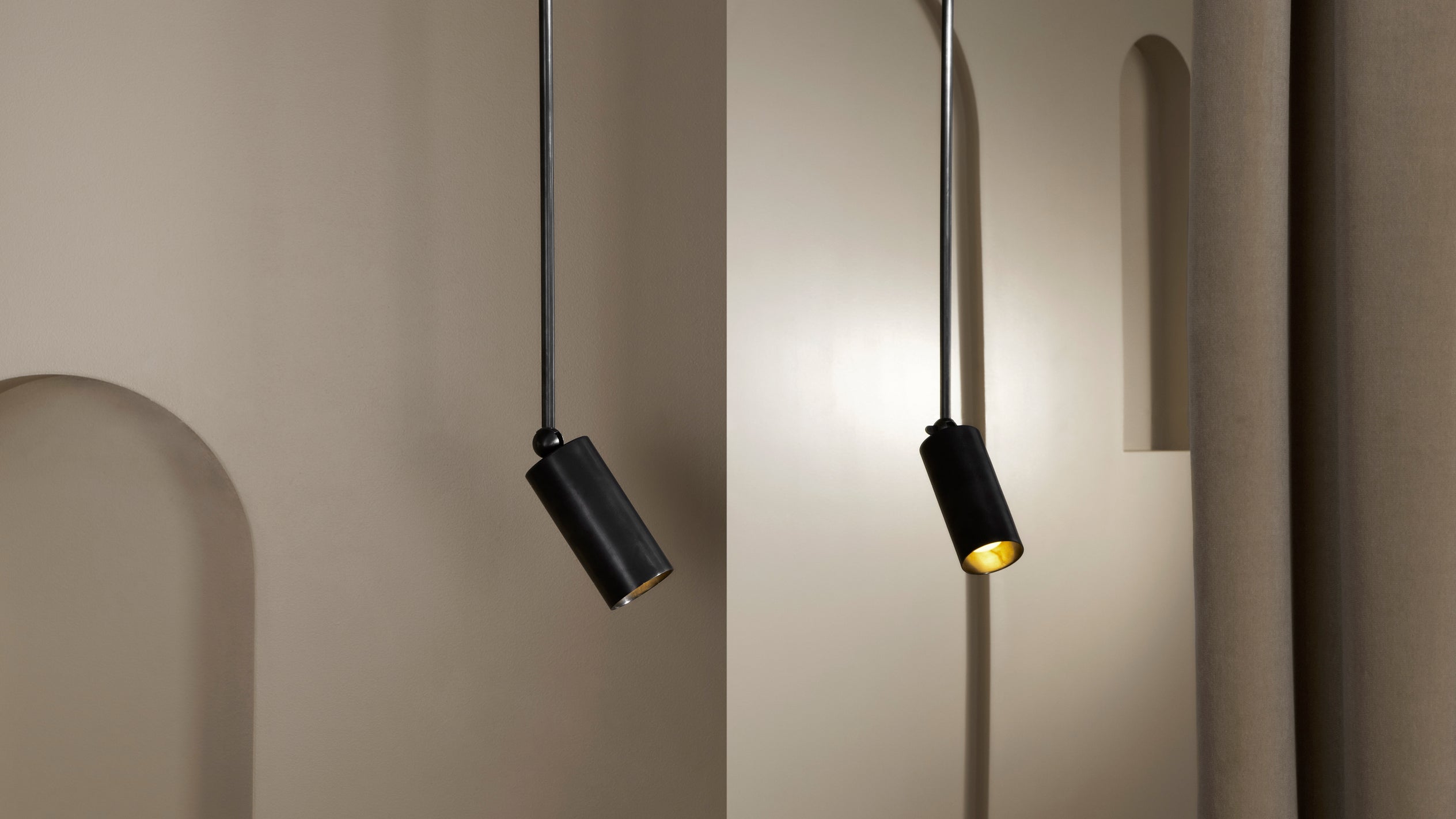 Two black cylindrical pendant lights casting soft warm light against a beige wall with arched details