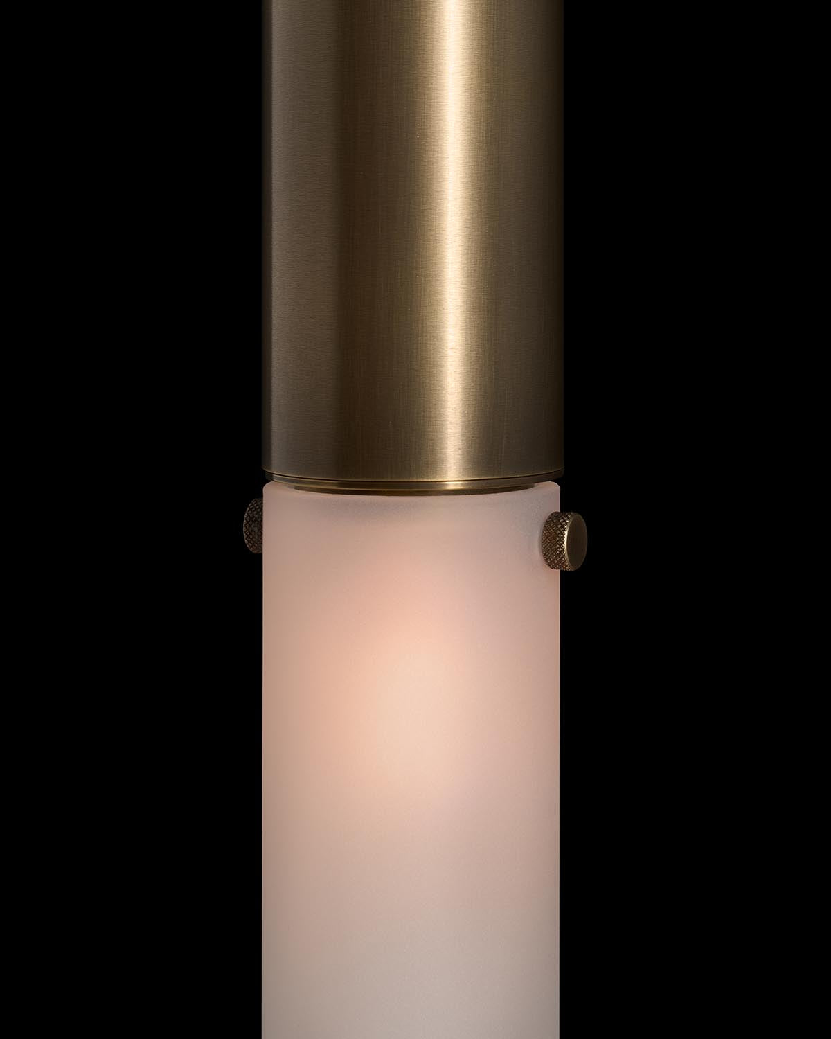 Close-up of a cylindrical wall sconce with brushed brass finish and frosted glass diffuser against black background