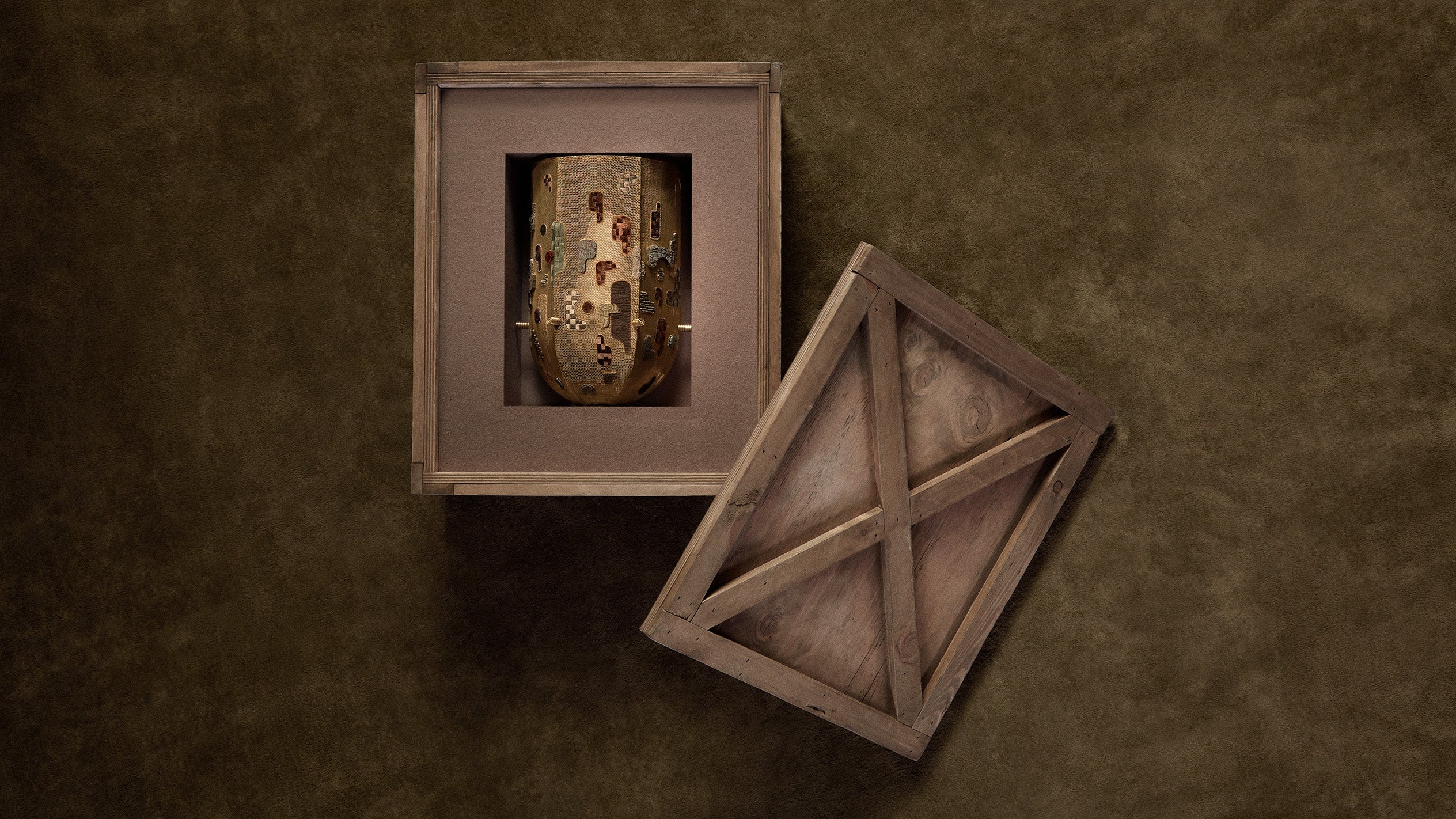 Top view of an antique wooden box with removable lid revealing a decorated ceramic vase inside on a textured brown surface