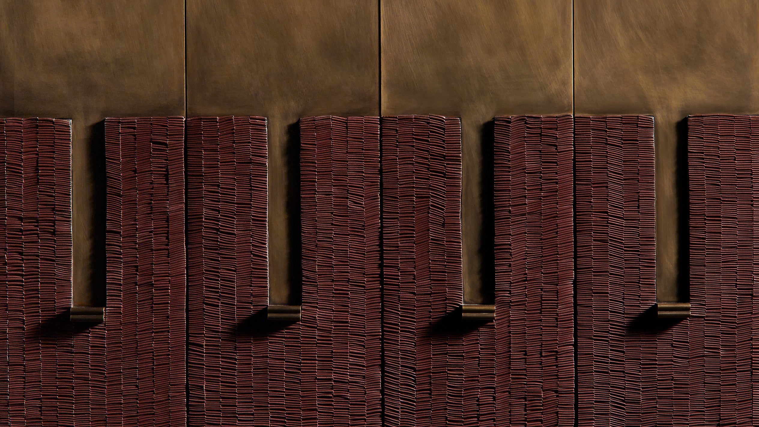 Close-up of a textured red brick wall with vertical sections casting shadows against a tan background