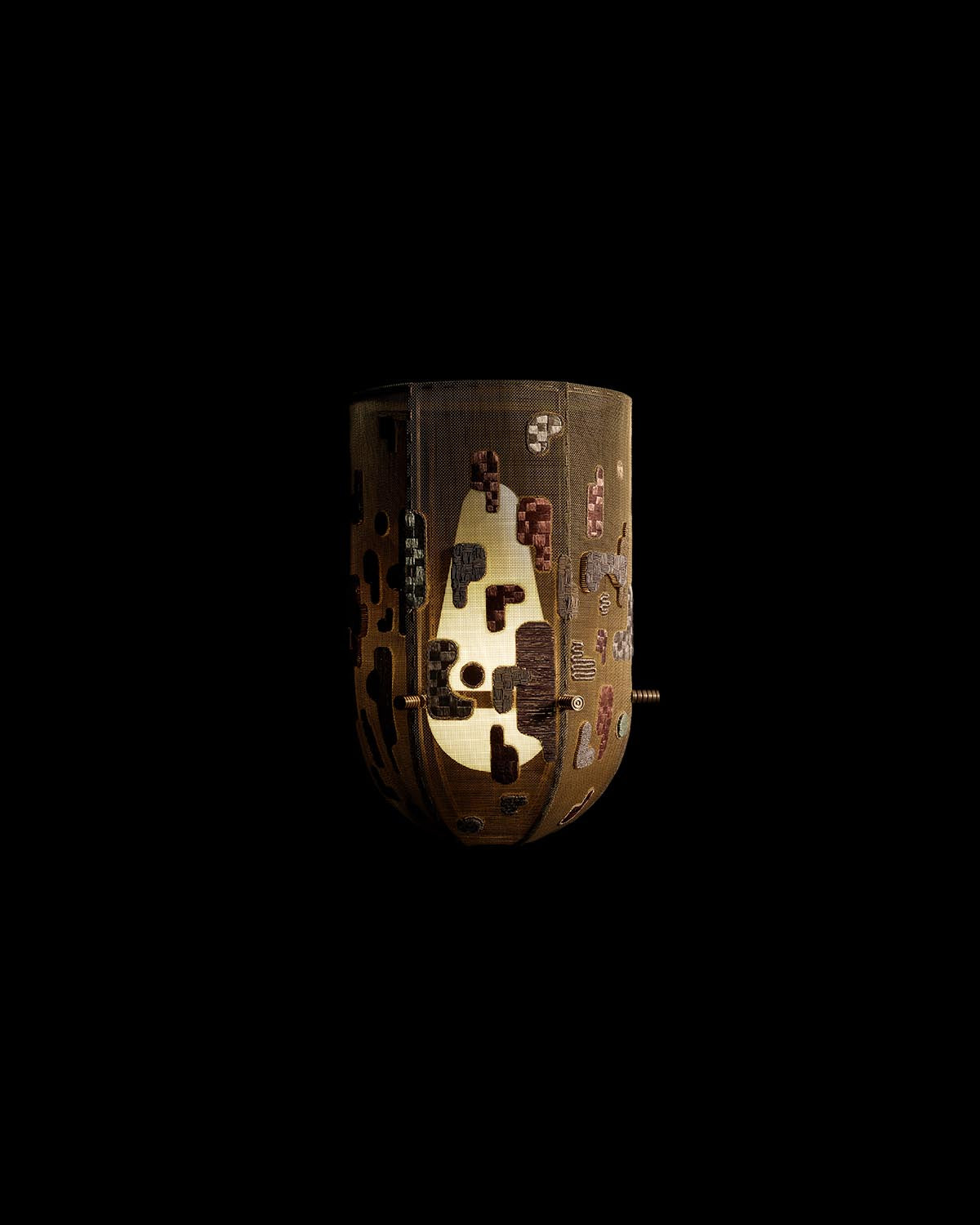 Close-up of a hand-embroidered metal sconce with intricate abstract patterns illuminated from within on a black background