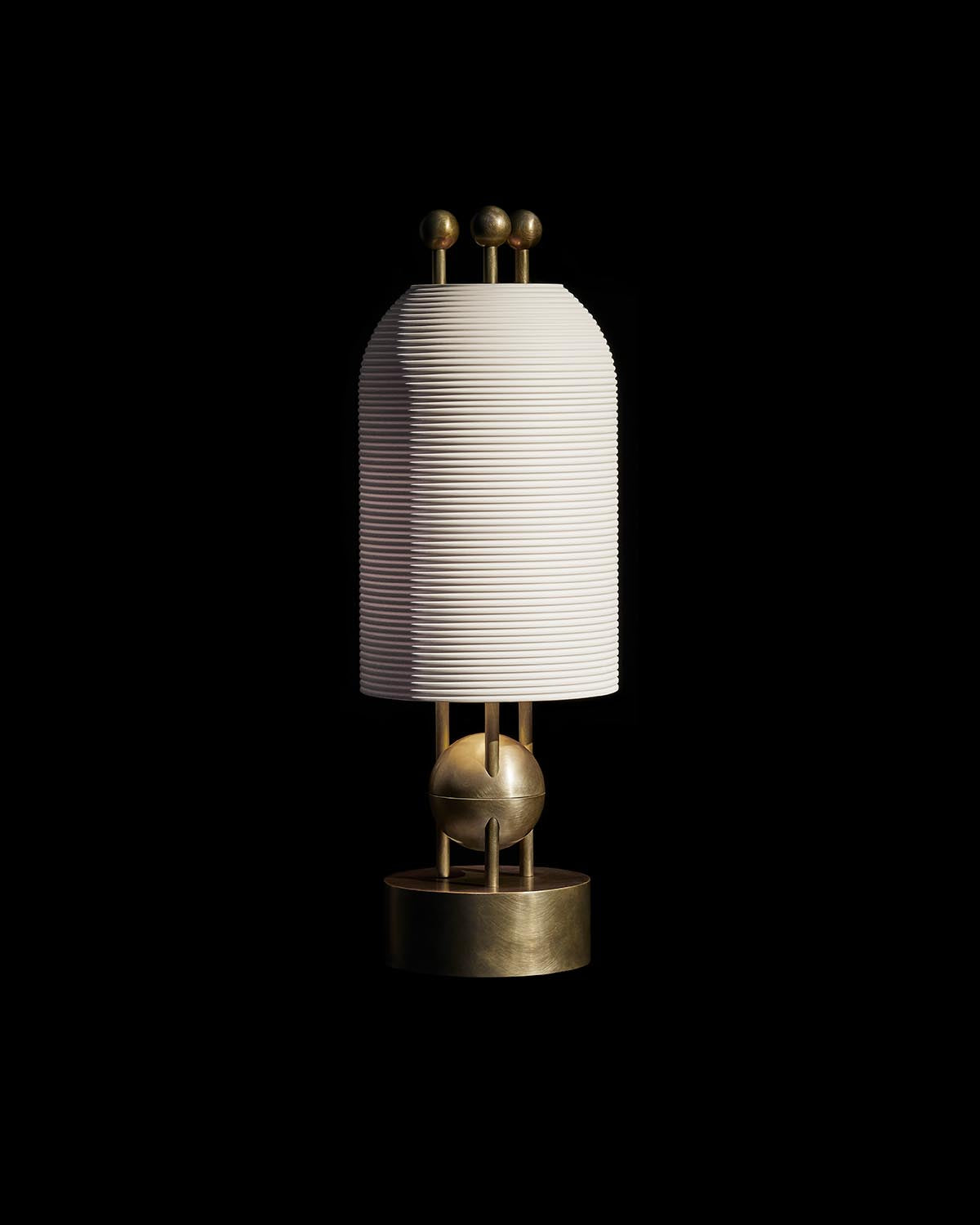 Modern table lamp with ribbed cylindrical shade and brass spherical accents on a reflective surface against black background