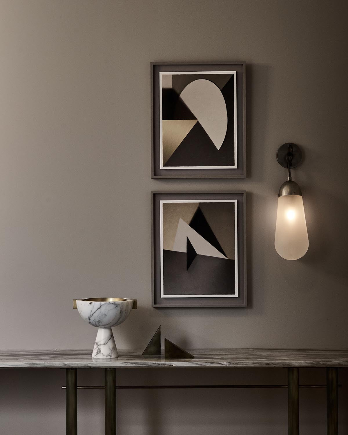 Minimalist wall sconce with frosted glass shade beside two abstract framed artworks above a marble-topped console table