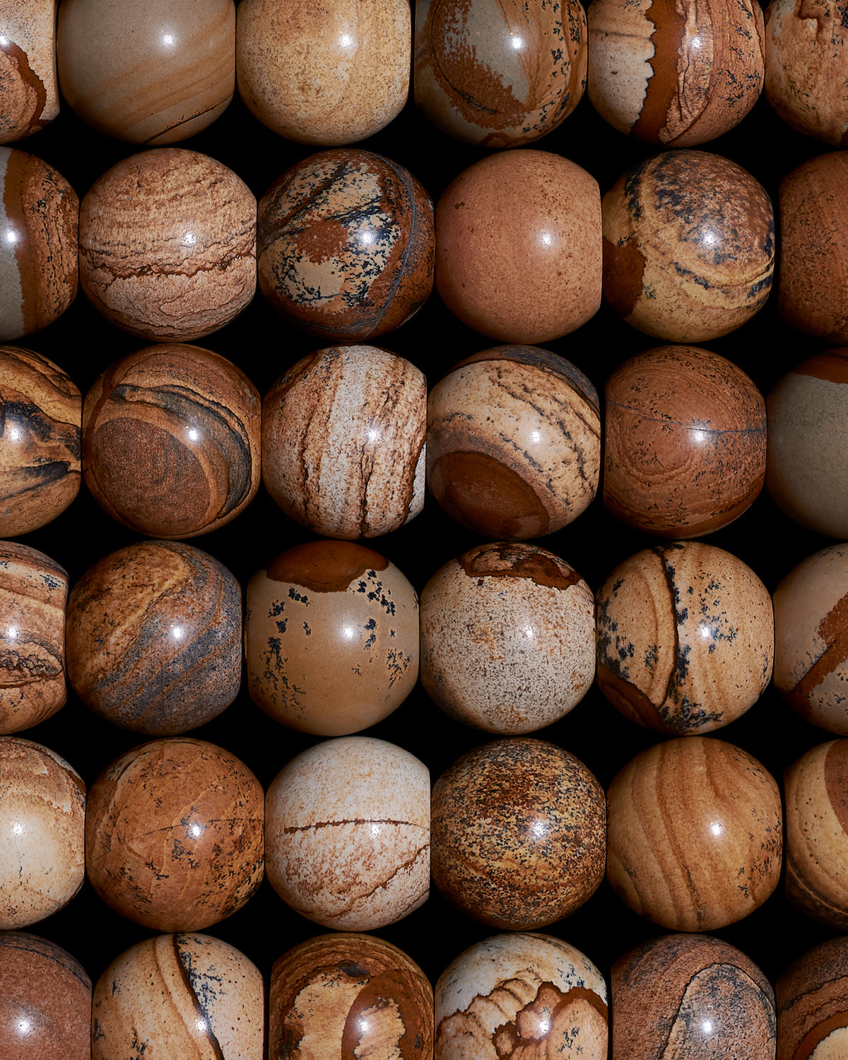 Close-up of multiple polished round stone spheres with natural beige, brown, and tan patterns arranged in rows on a black background
