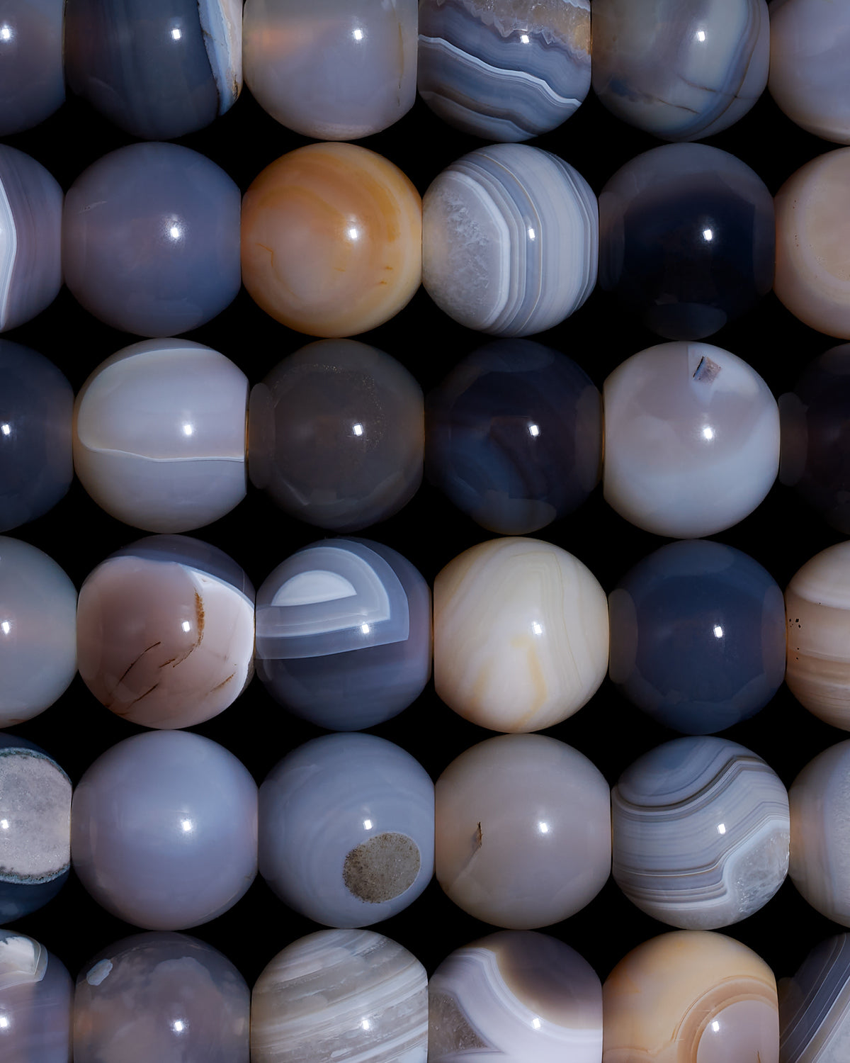 Close-up of polished round stones in muted gray and beige tones arranged in a grid pattern on a dark background