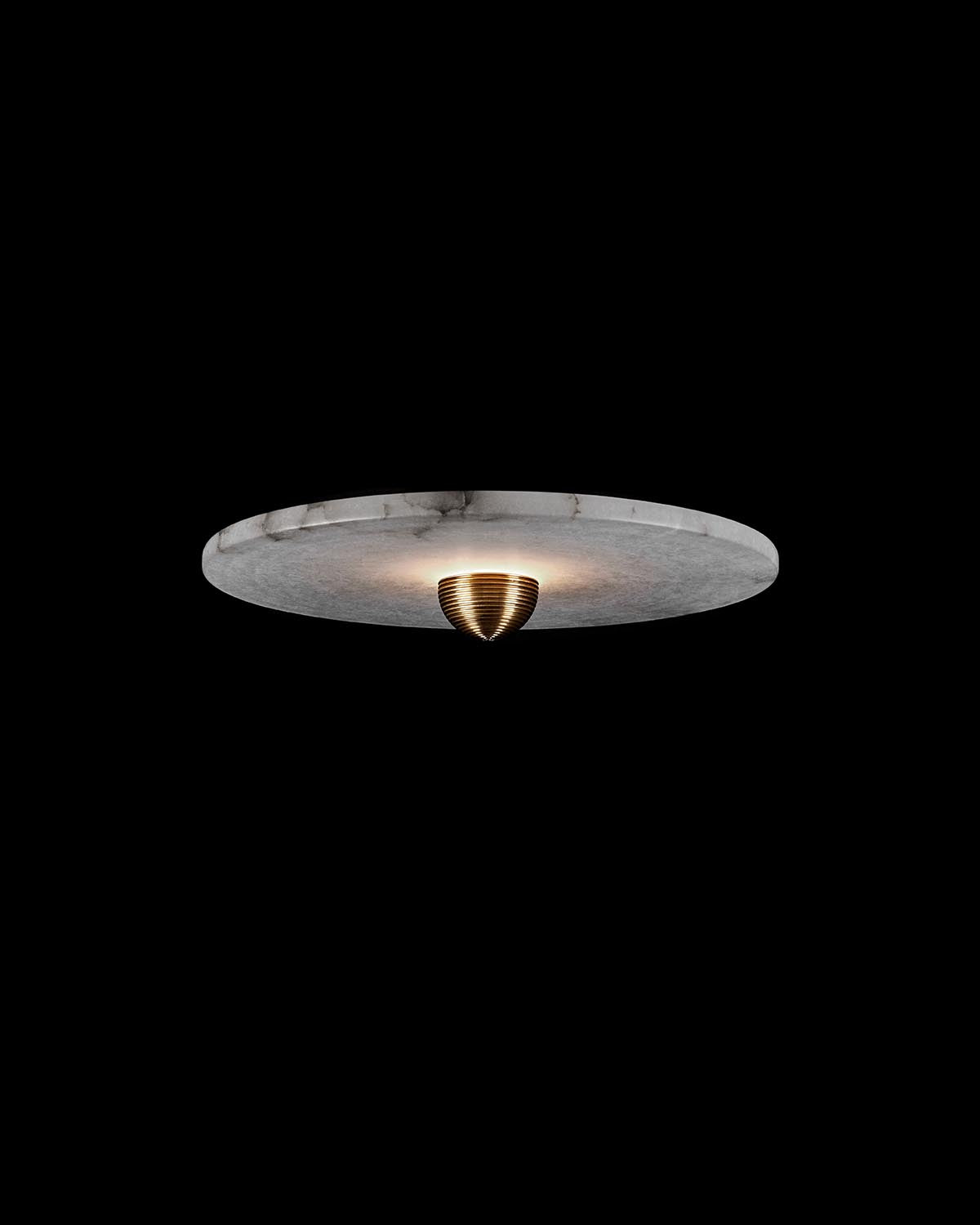 Round white marble surface with subtle veining and a conical brass centerpiece against black background