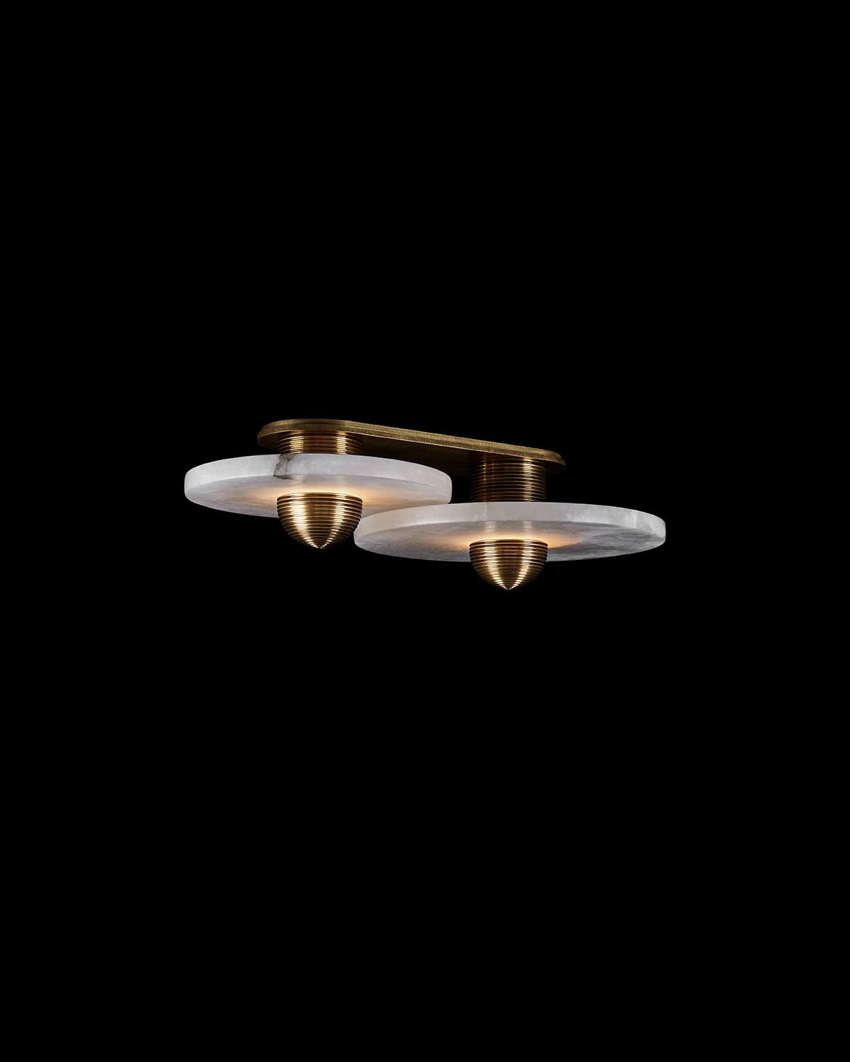 Close-up of a dual circular alabaster light fixture with brass accents against a black background