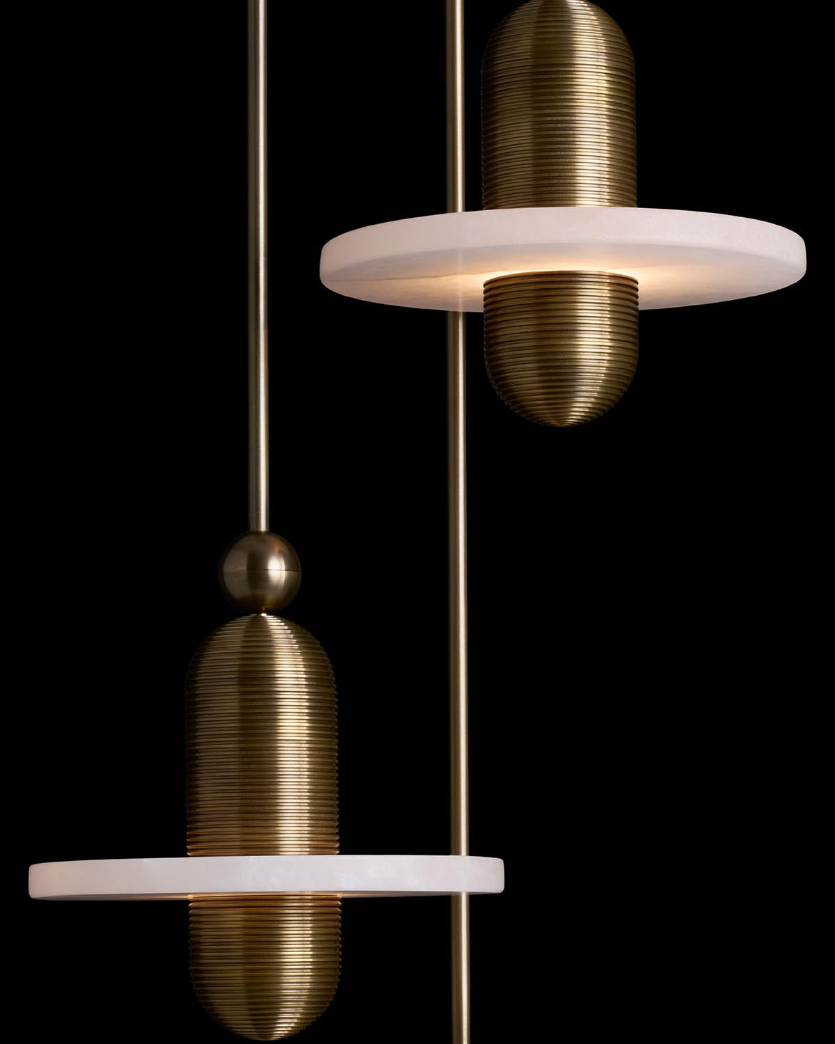 Close-up of MEDIAN 3 pendant lights with ribbed brass elements and white circular plates on dark background