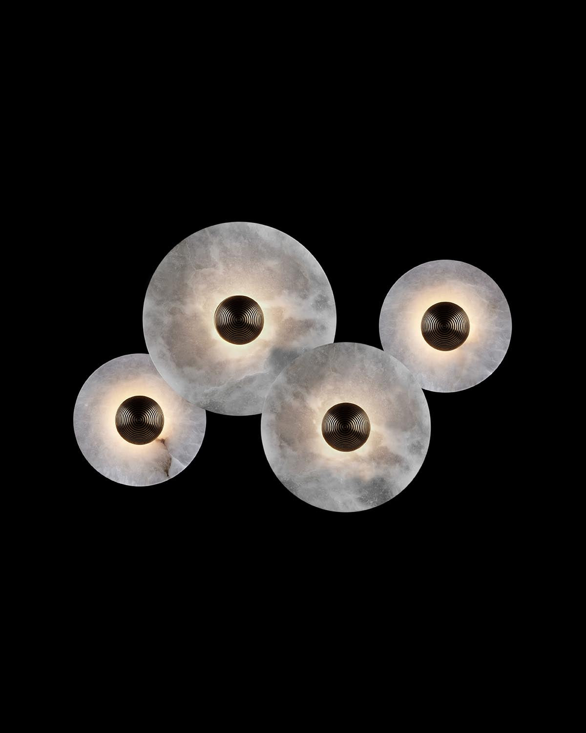 Cluster of four round marble light fixtures with dark textured centers glowing softly against black background