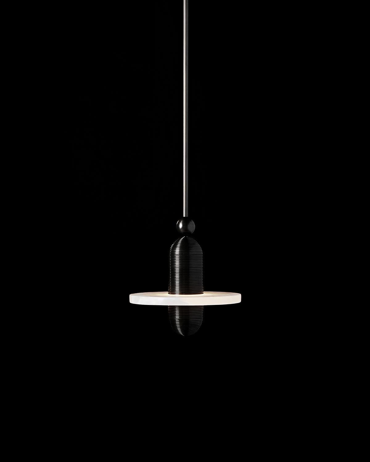 Minimalist black pendant light with a ribbed cylindrical body and flat round white diffuser against a black background