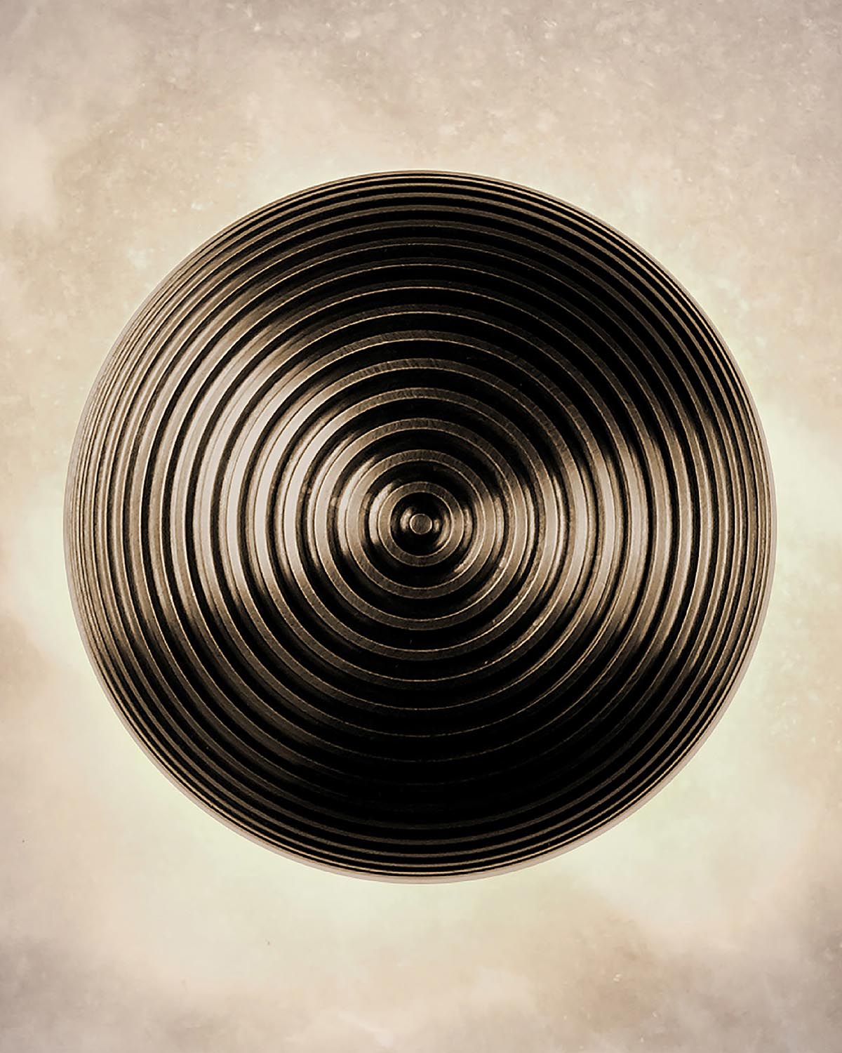 Top-down view of a round surface with concentric circular ridges in dark metallic finish on a neutral background