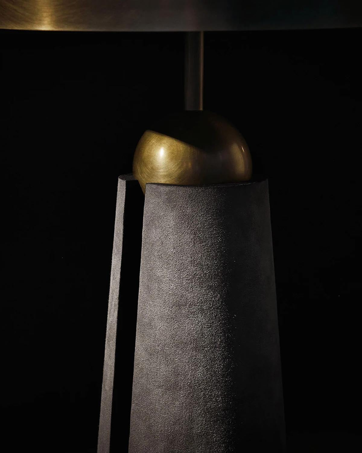 Close-up of the METRONOME floor lamp base with textured dark gray surface and smooth bronze spherical detail against black background