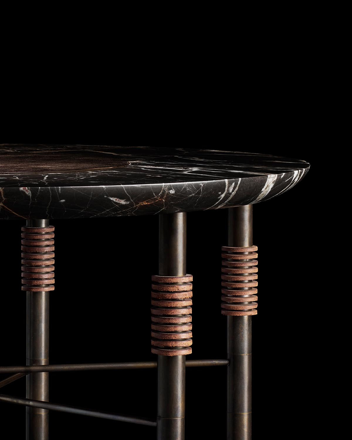 Close-up of round dark marble tabletop with metal legs featuring stacked rust-colored disc accents on black background