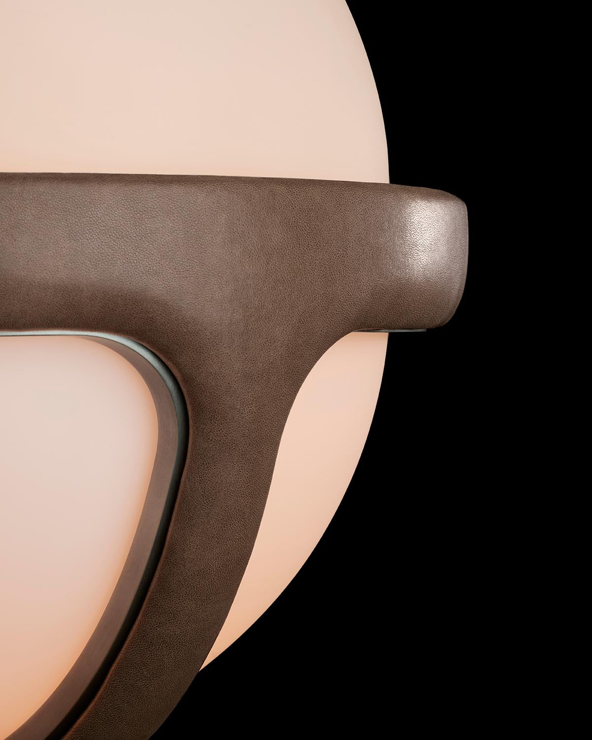 Close-up of a dark brown textured leather sconce arm against a soft glowing circular light background