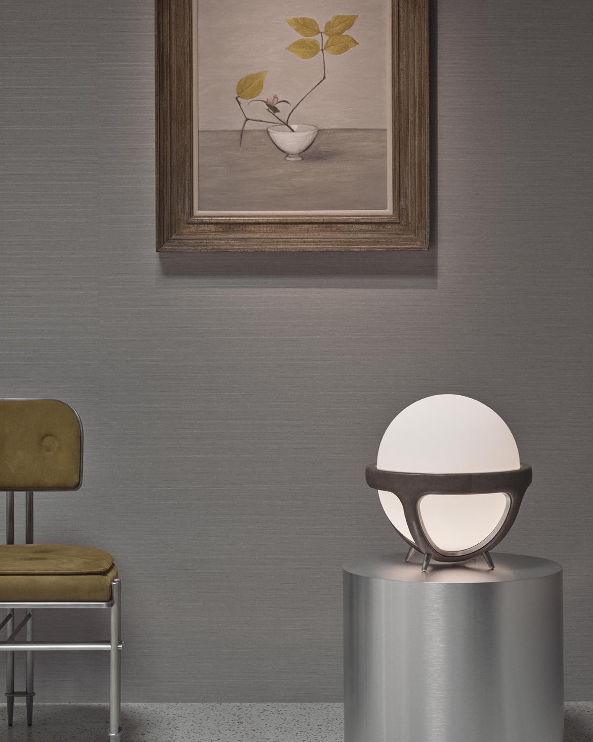 Glowing spherical table lamp with dark metal frame on a metallic cylindrical pedestal against a textured gray wall