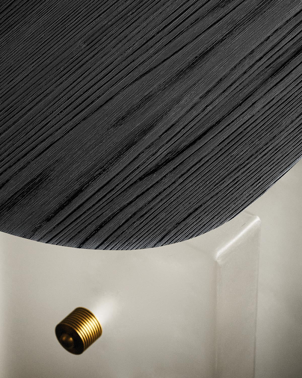 Close-up of a round side table with textured dark wood top and smooth light-colored base with a small brass detail