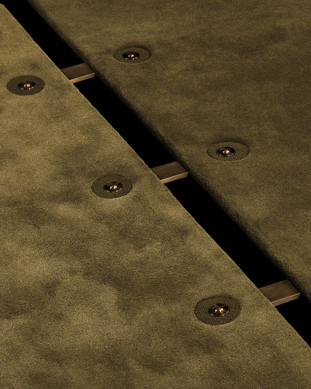 Close-up of olive green suede panels with round metal button accents and visible brass connectors on black background
