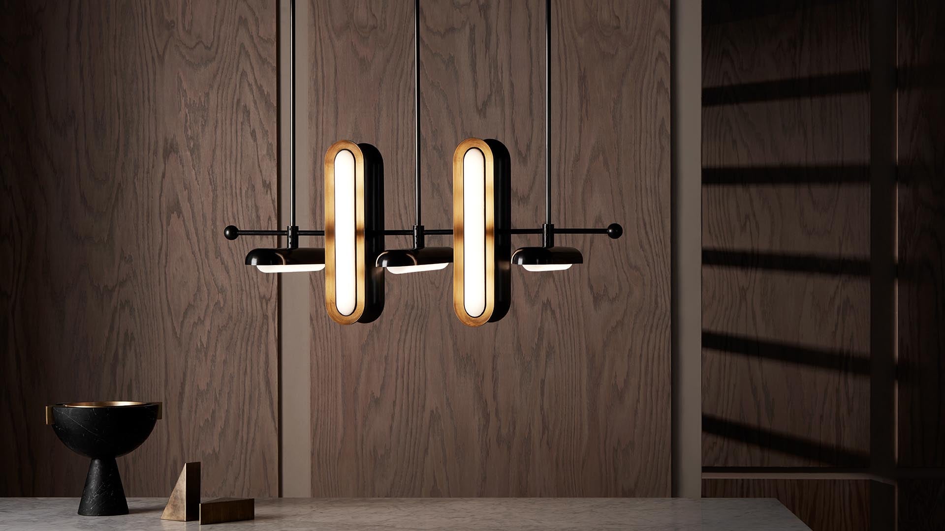 Contemporary black and brass pendant lights with elongated oval shapes hanging before a dark wood paneled wall above a stone surface.