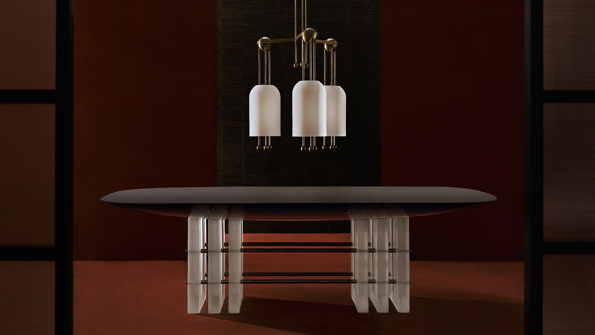 Oval dark tabletop supported by sculptural vertical panels with bronze rods, under a cluster of white pendant lights