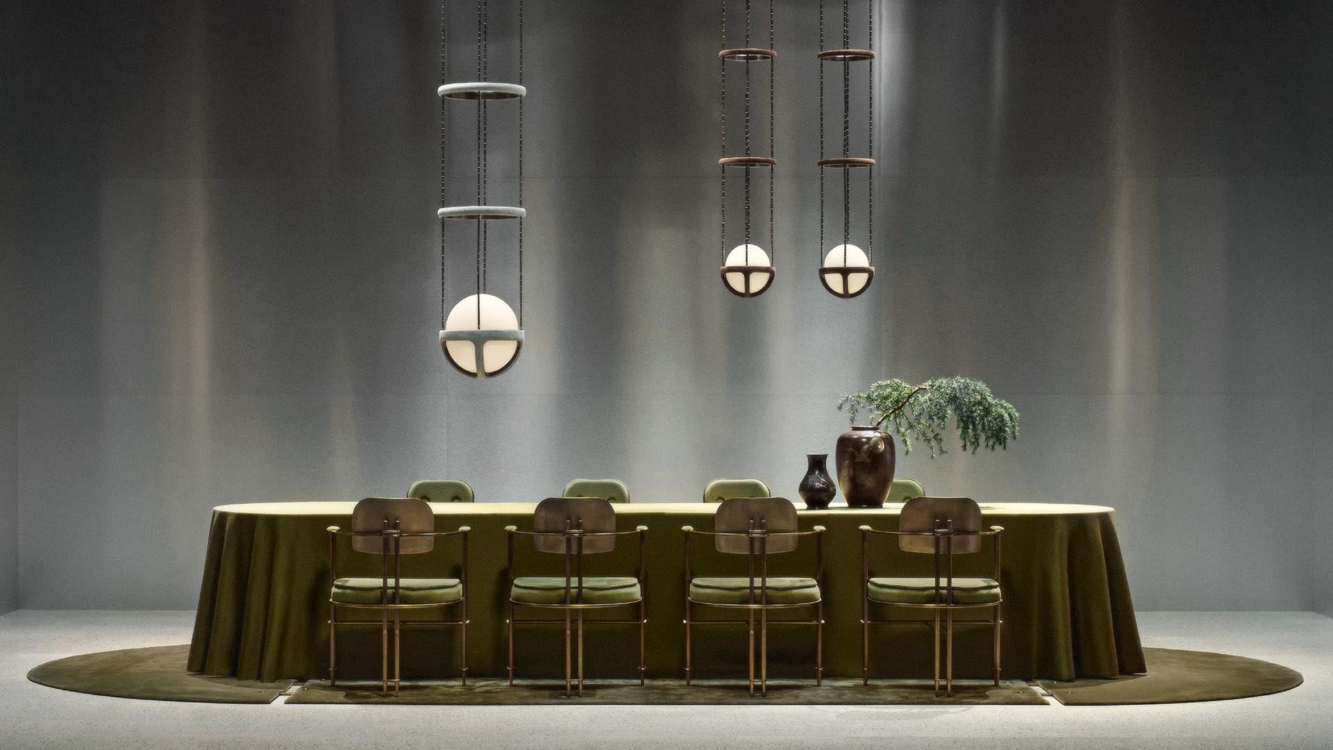 Long oval dining table with olive green tablecloth, six metal chairs, decorative vases, and three pendant lights above