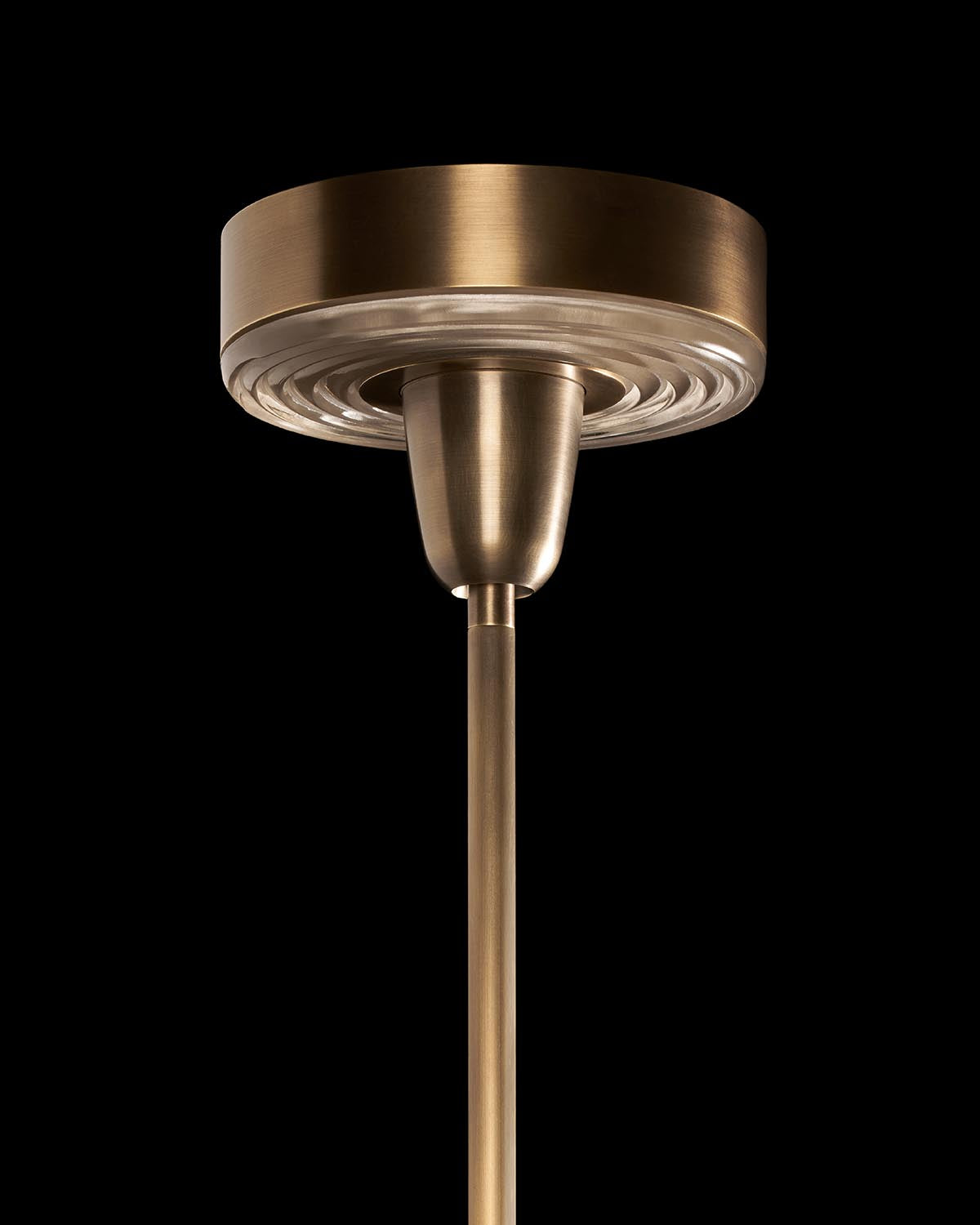 Close-up of brass-finished pendant light canopy and rod with circular glass diffuser against black background