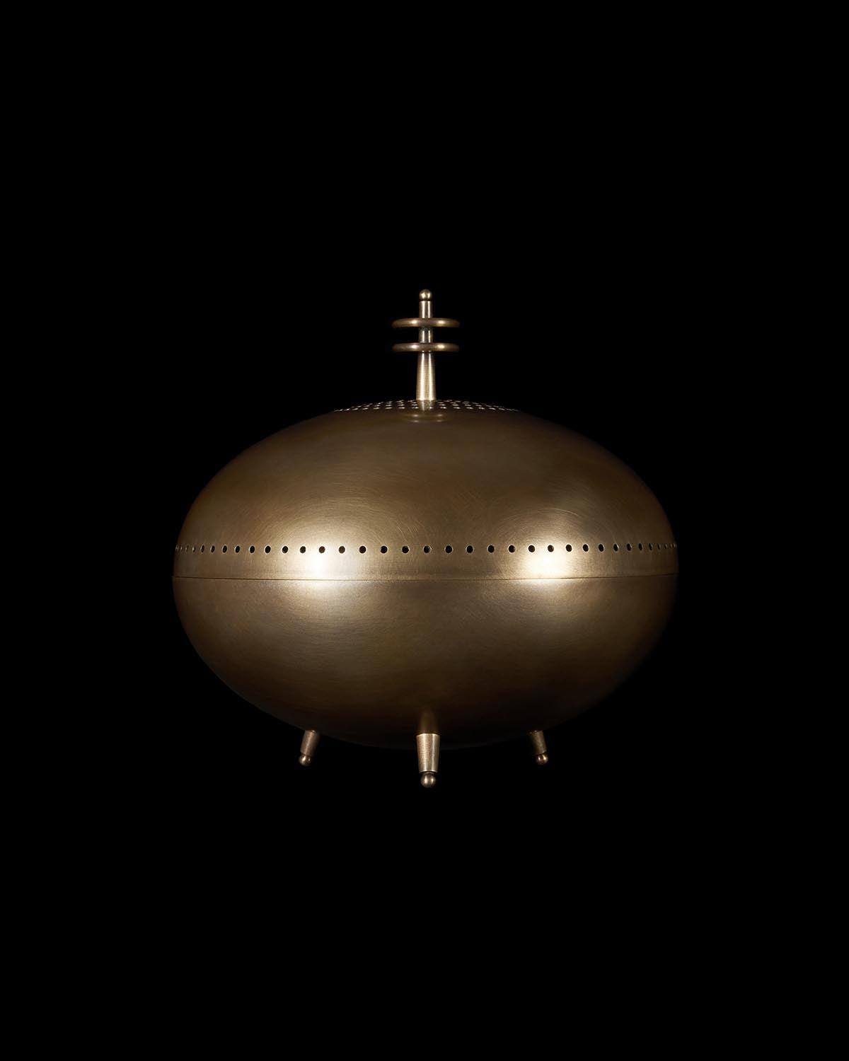 Oval bronze smoking vessel with perforated midsection and small round legs against a black background