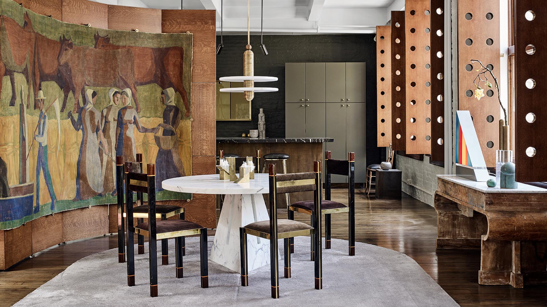 Dining area with round white table surrounded by wooden chairs, mural backdrop, and large windows with wooden frames and exposed bolts