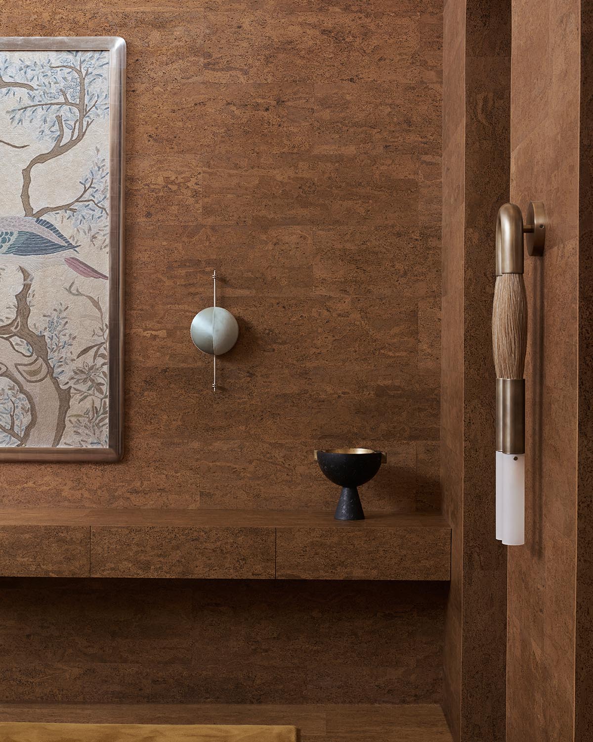 Interior corner with textured brown walls, a framed bird artwork, a metallic wall sculpture, and a black pedestal bowl on a floating shelf
