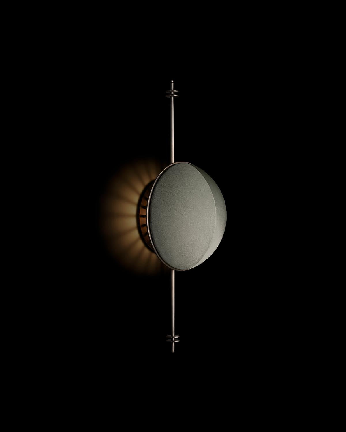 Minimalist wall sconce with a round, textured front and thin vertical metal rod, casting soft light on a dark background