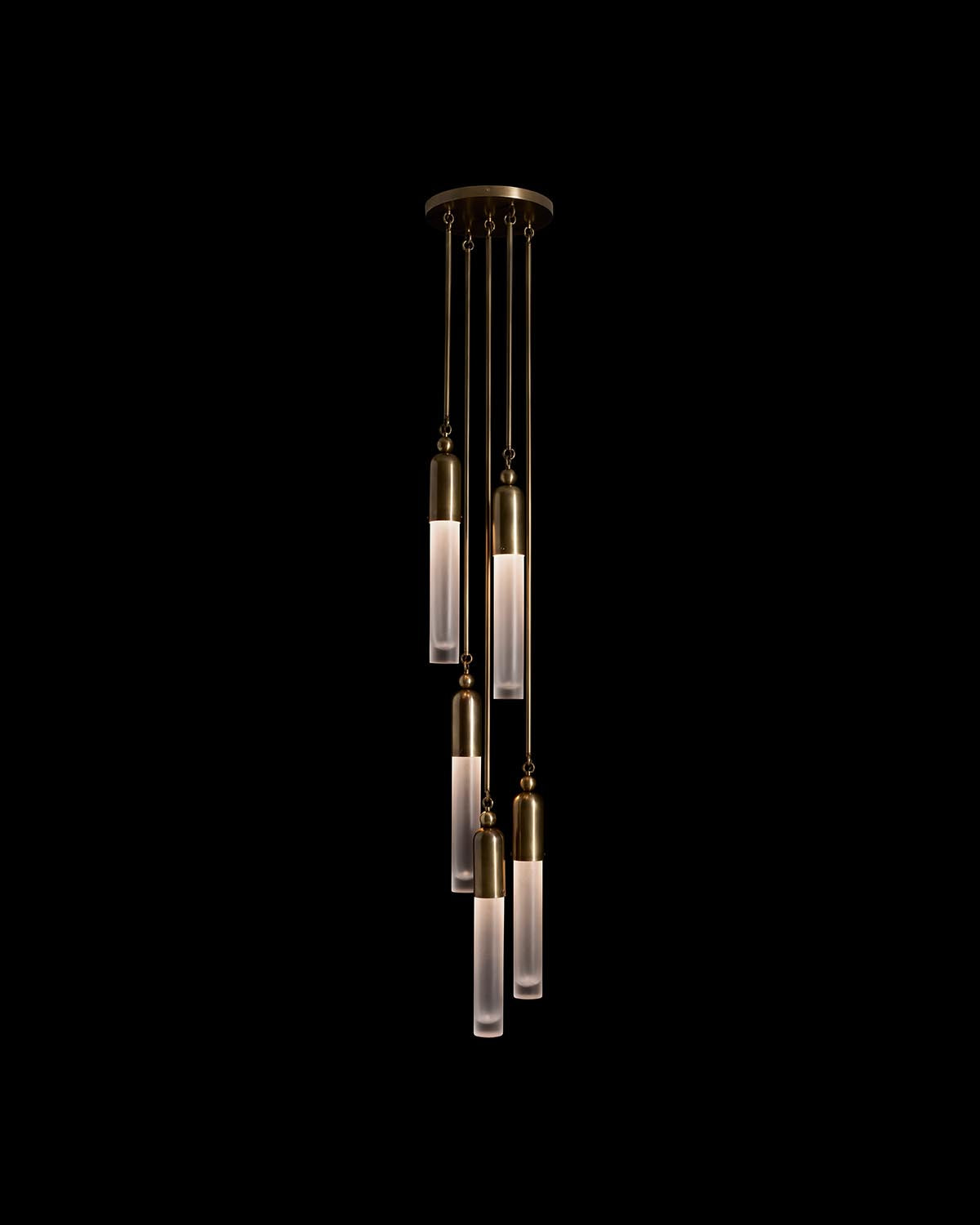 Cluster of five slender pendant lights with frosted glass cylinders and brass fittings suspended against black background