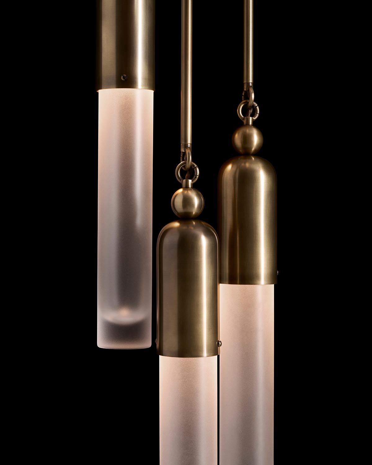 Three elongated pendant lights with frosted glass housings and brushed brass cylindrical caps against black background
